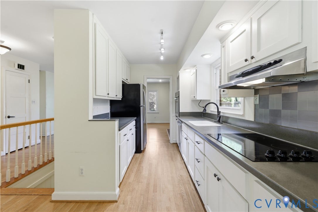 Galley kitchen with white cabinetry, black countertops, wood-finish flooring, and a stainless steel range hood