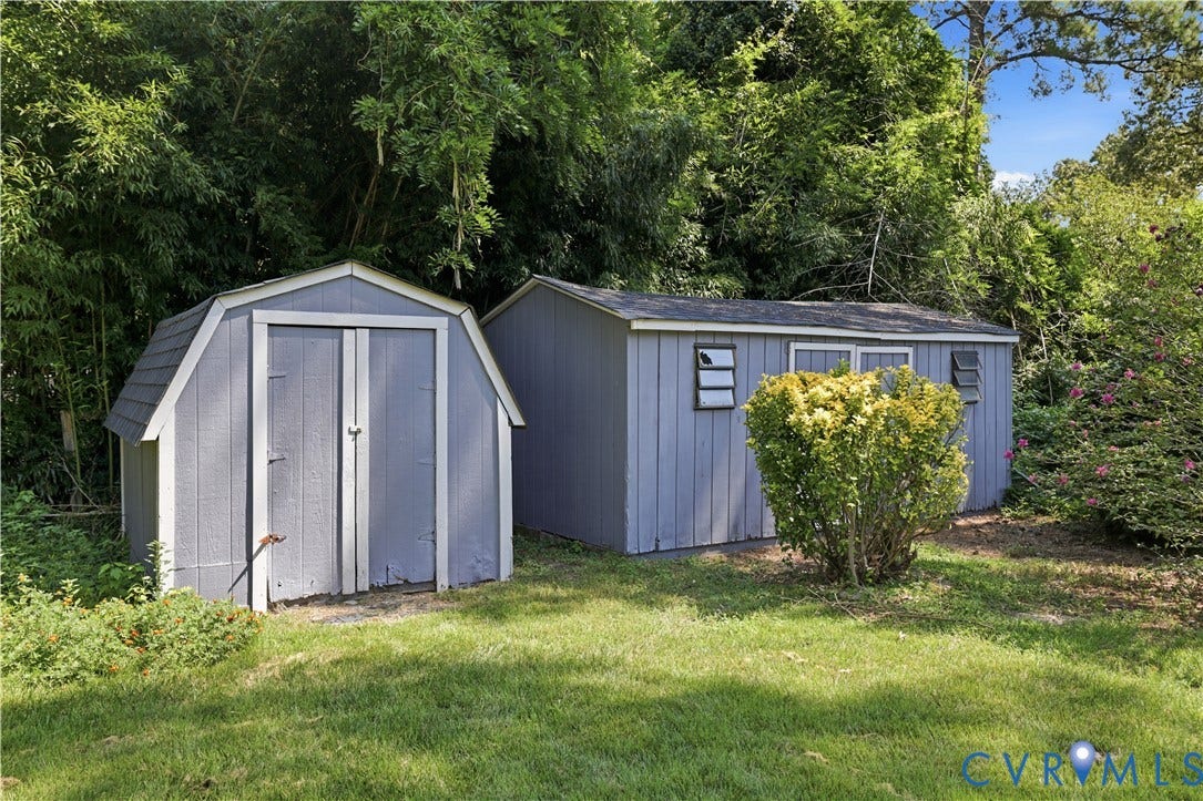 Two exterior storage sheds, one with a gambrel roof and double doors, and another with multiple windows