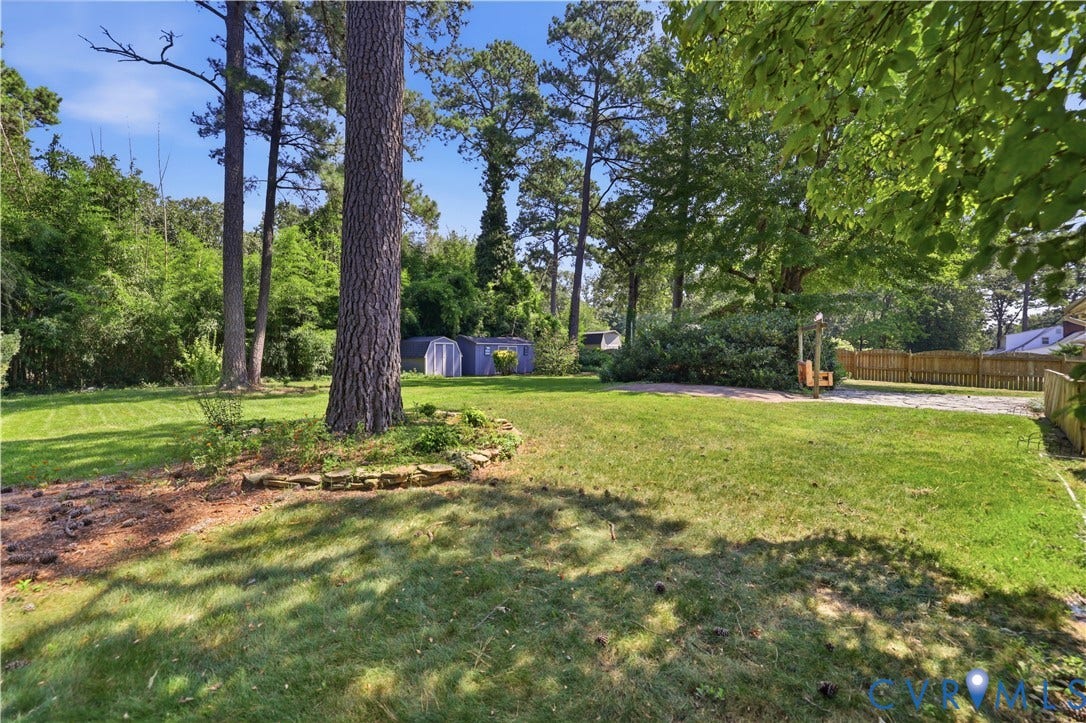 Expansive green lawn with mature trees and a wood fence