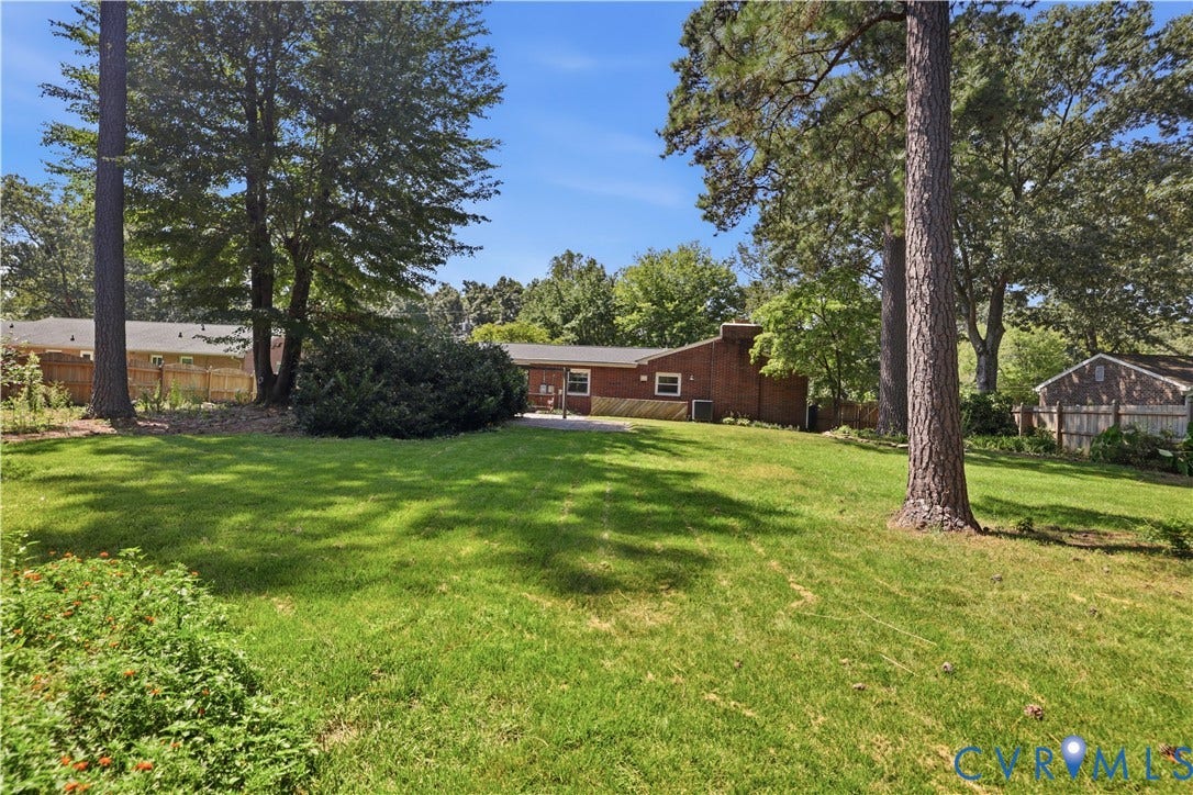 Expansive green lawn with mature trees, a brick exterior, and a detached outbuilding