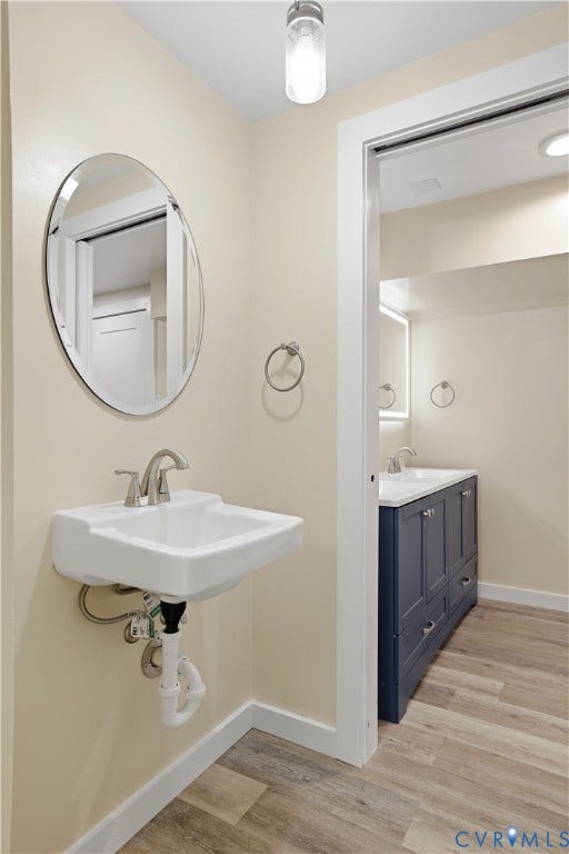 Wall-mounted sink with brushed nickel faucet, oval frameless mirror, and wood-finish flooring