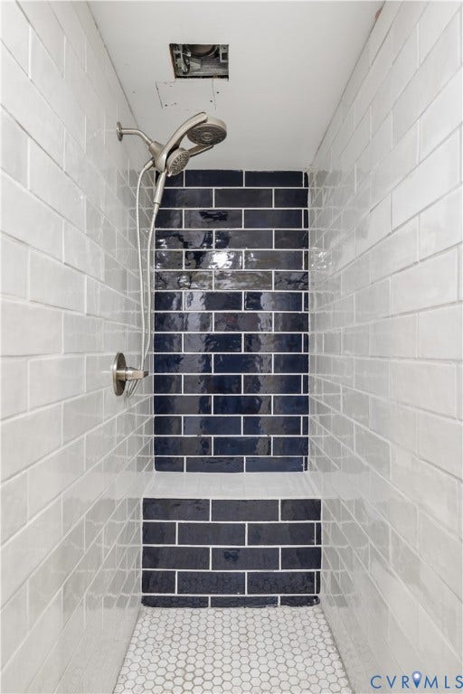 Walk-in shower with white subway tile walls, a dark blue accent tile, a built-in shower bench, and a brushed nickel shower head