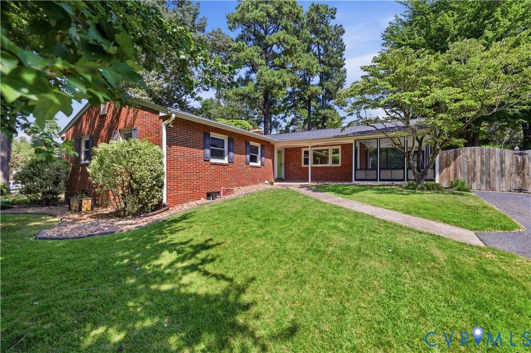 Brick exterior with dark shutters, established landscaping, front walkway, and a paved driveway