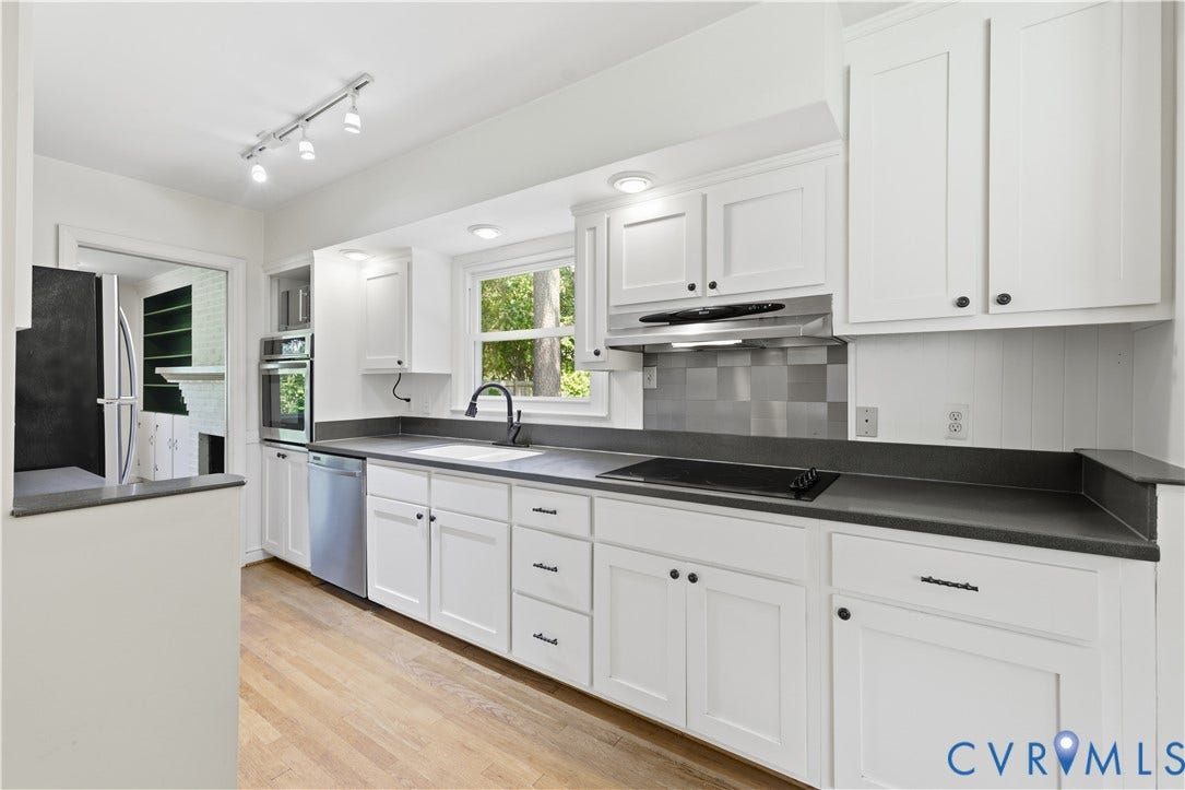 White shaker cabinetry, dark countertops, integrated cooktop, stainless steel dishwasher, and wood-finish flooring
