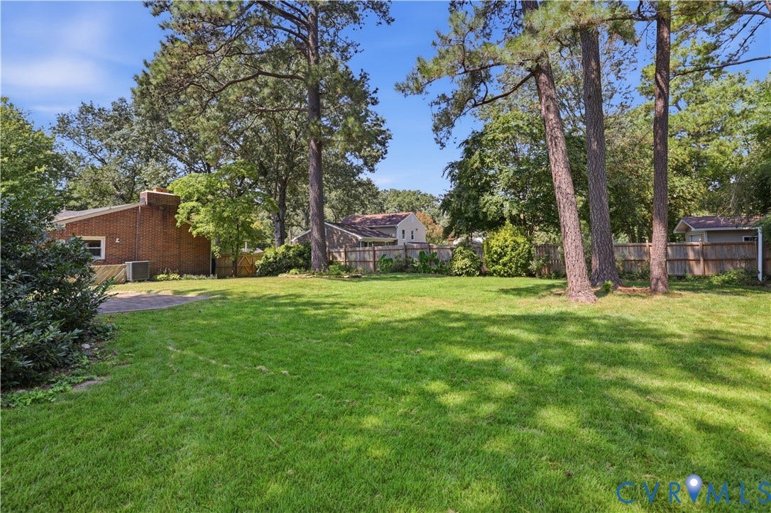 Expansive green lawn framed by mature trees, a wood privacy fence, and a brick exterior structure
