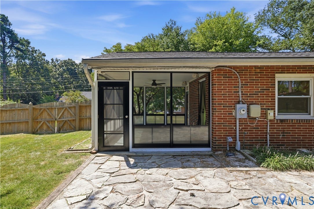 Enclosed porch with large windows, exterior brick finish, stone patio, and fenced yard