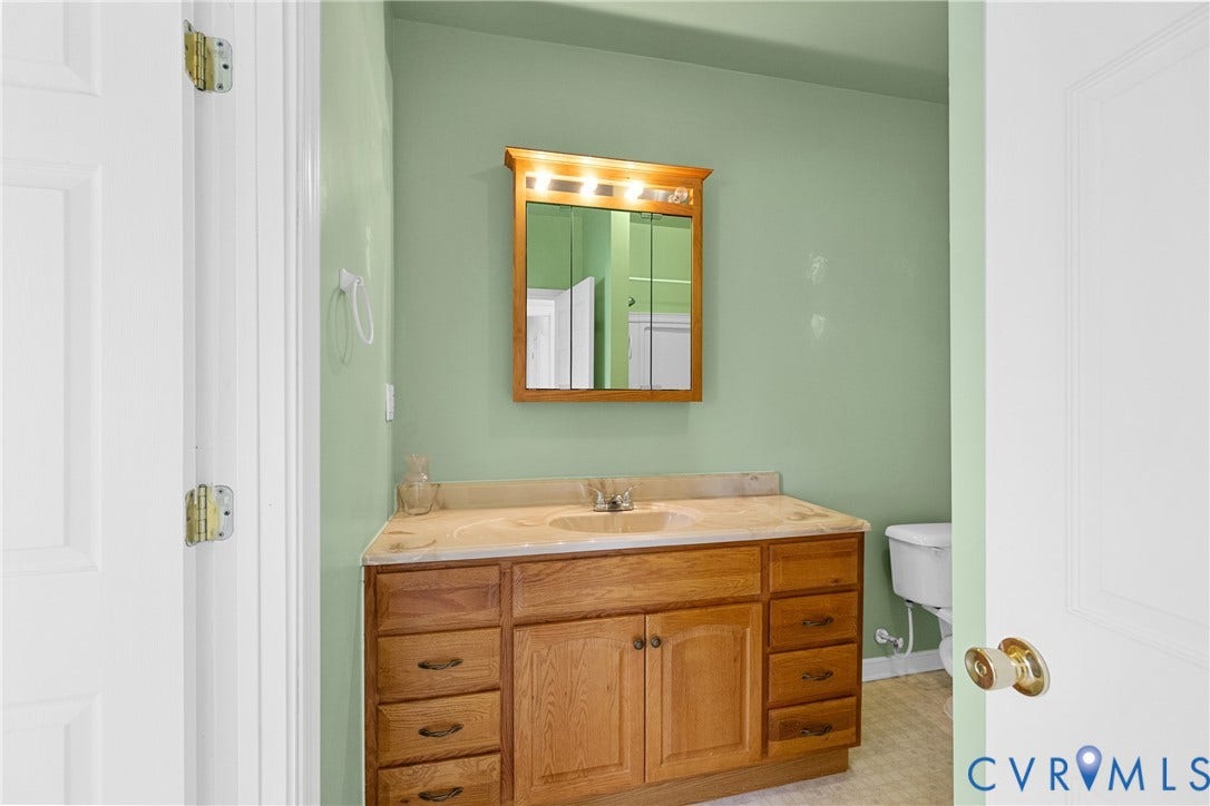 2314 Ingram Avenue, Richmond, VA 23224 Wood-finish vanity with an integrated sink and light-toned countertop, framed mirror with overhead lighting, and a white toilet