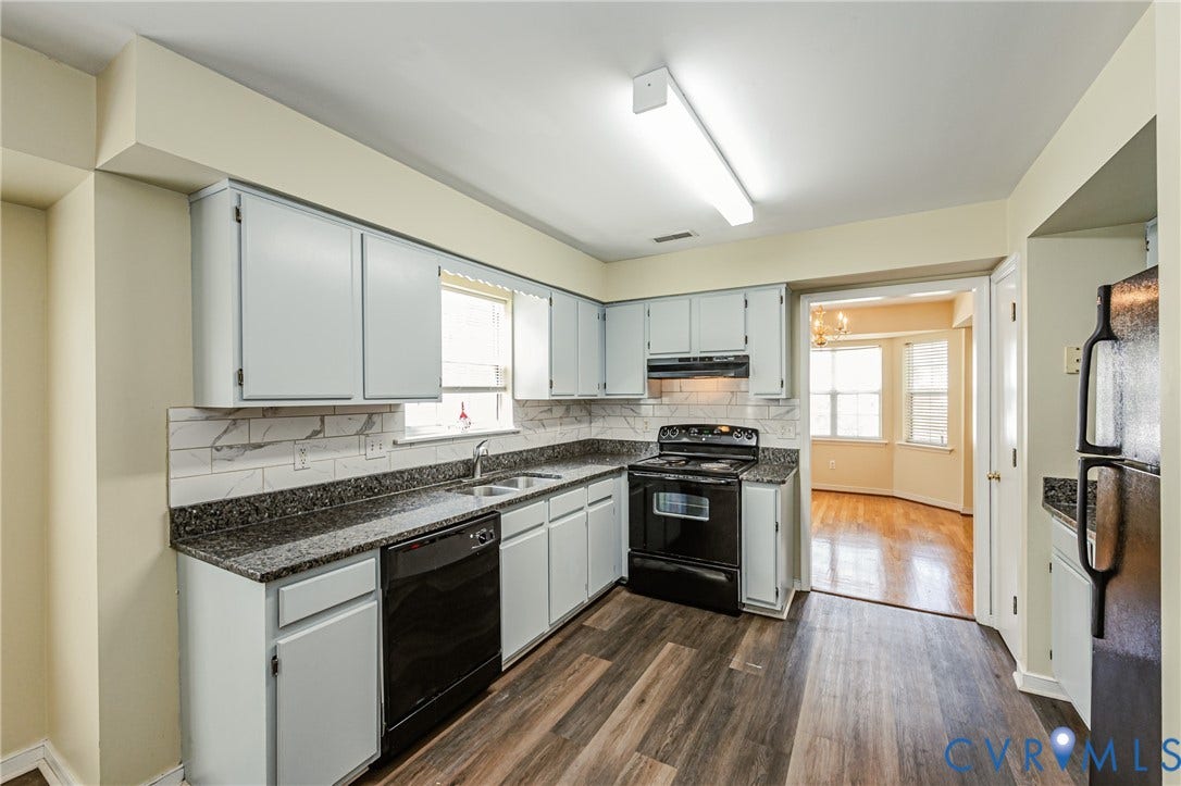 Kitchen featuring wood-finish flooring, dark countertops, white subway tile backsplash, and light-colored cabinetry