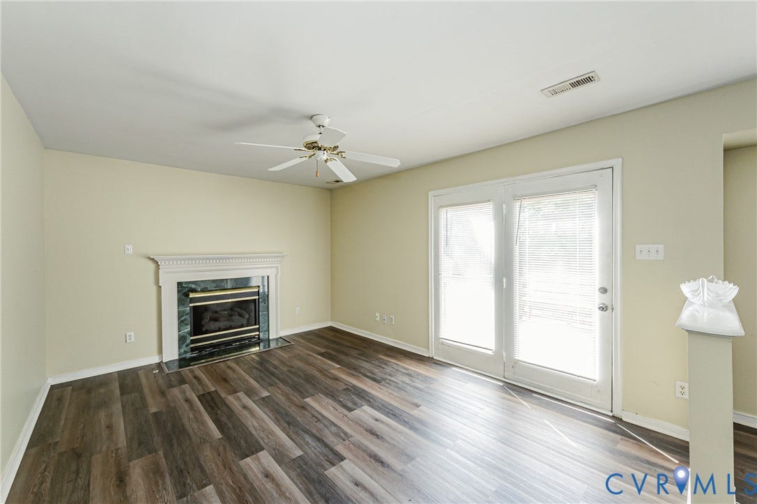 Living area featuring wood-finish flooring, a fireplace with a decorative mantel and stone surround, and a ceiling fan