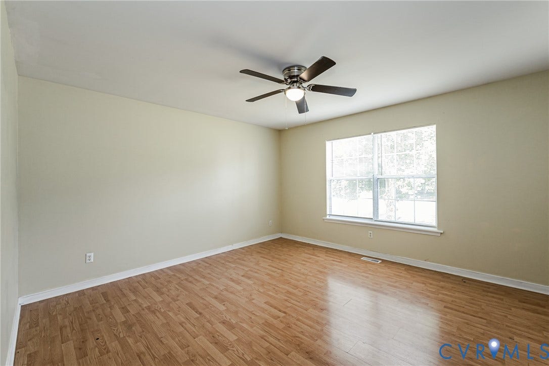 Wood-finish flooring, neutral wall paint, overhead ceiling fan with lighting, and a large window with white trim