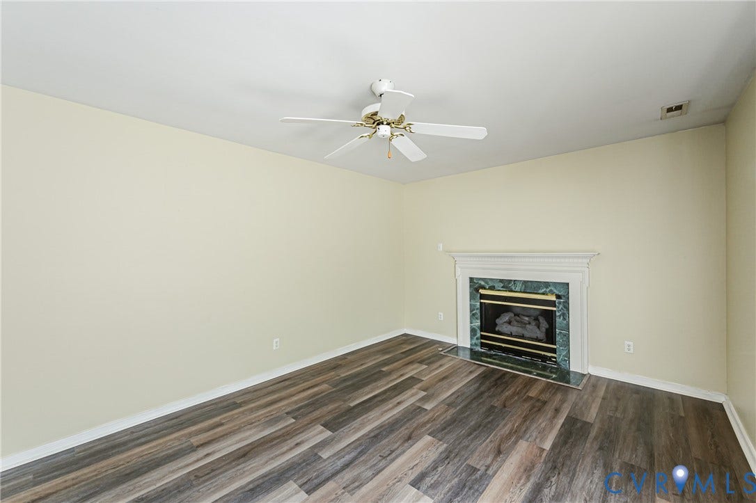 Vaulted ceiling featuring a ceiling fan, wood-finish flooring, and a fireplace with a stone surround and a white mantel