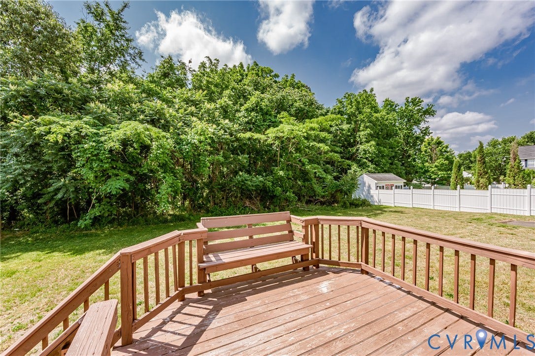 Expansive wood deck with built-in seating, offering a private backyard setting with a white privacy fence and a storage shed