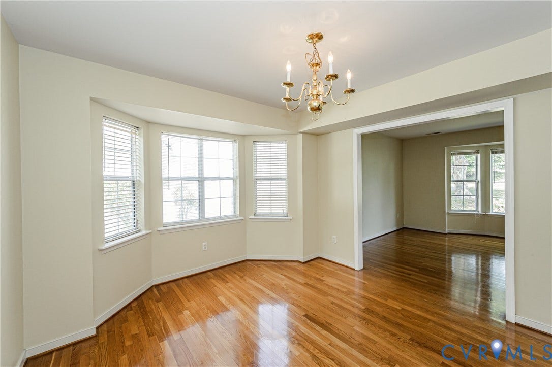 Hardwood flooring, bay window, white window blinds, brass chandelier, and an arched doorway