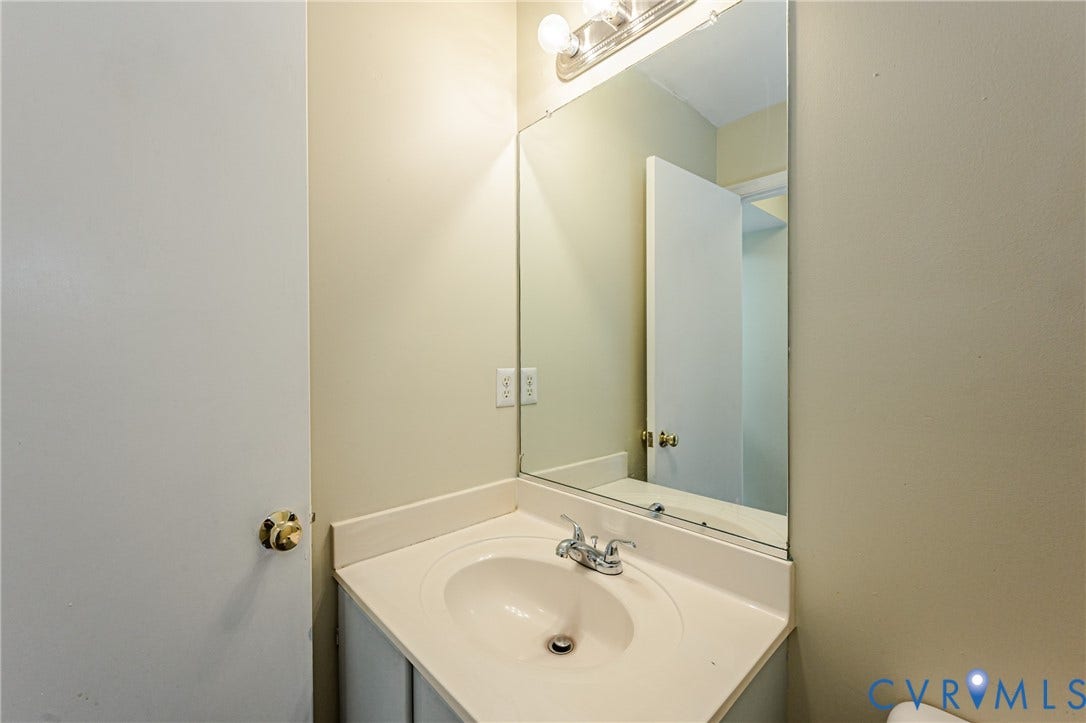 Corner vanity with integrated sink, chrome faucet, wall-mounted mirror, and overhead vanity lighting