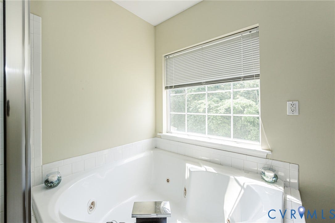 Built-in soaking tub with white tile surround and a window with blinds