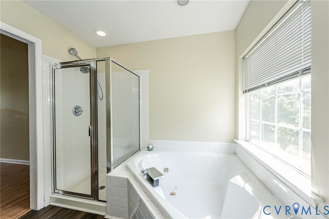 Walk-in shower with glass enclosure, corner soaking tub, and a window with blinds