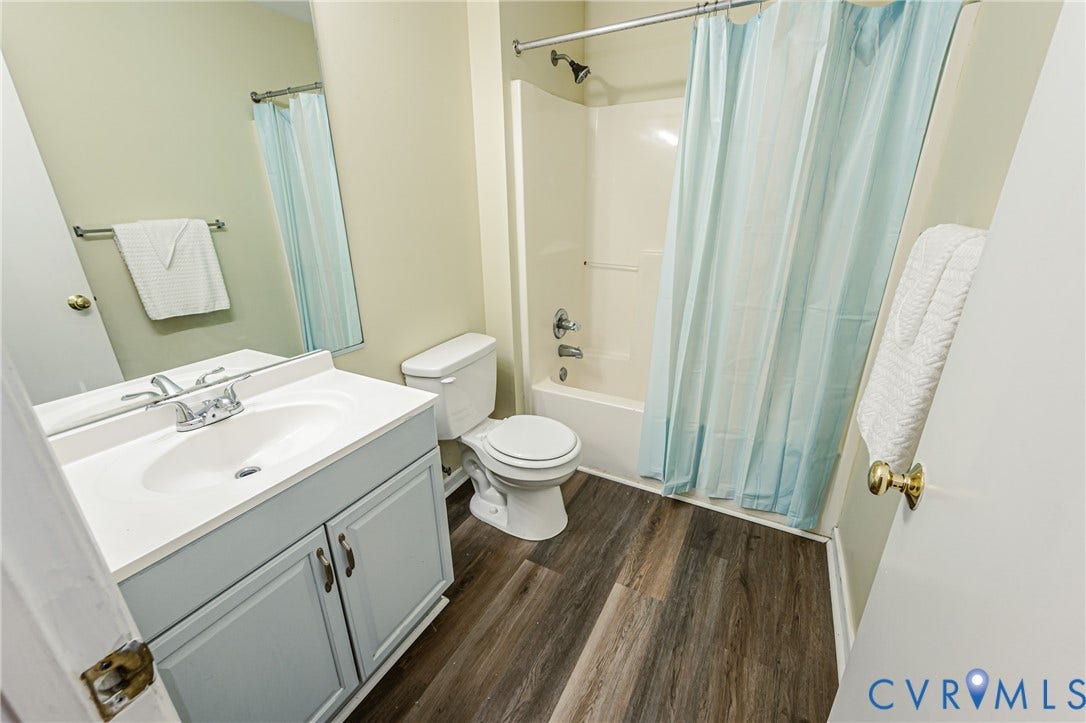 Vanity with integrated sink and chrome faucet, wood-finish flooring, and a tub-shower combination