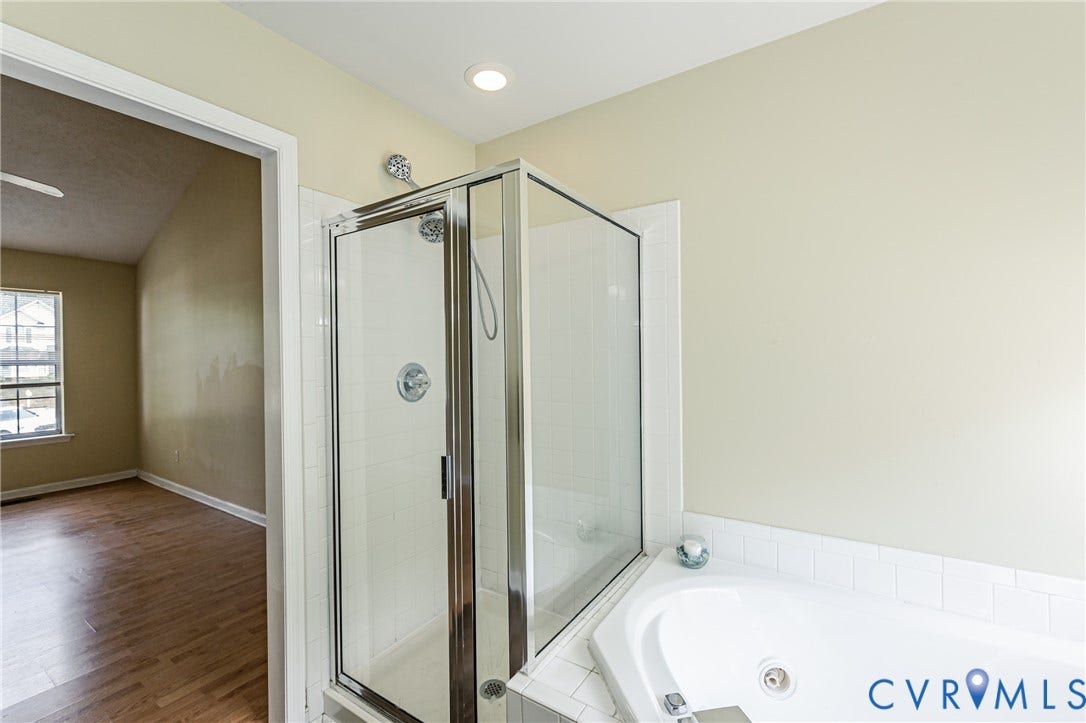Recessed lighting, tile-surround corner bathtub, glass-enclosed shower, chrome shower fixtures, and wood-finish flooring