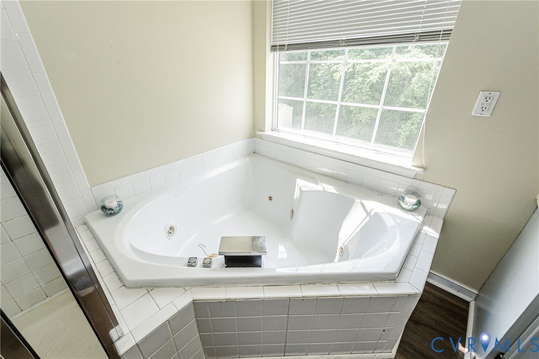 Built-in jetted tub surrounded by white tile, with a large window and wood-finish flooring