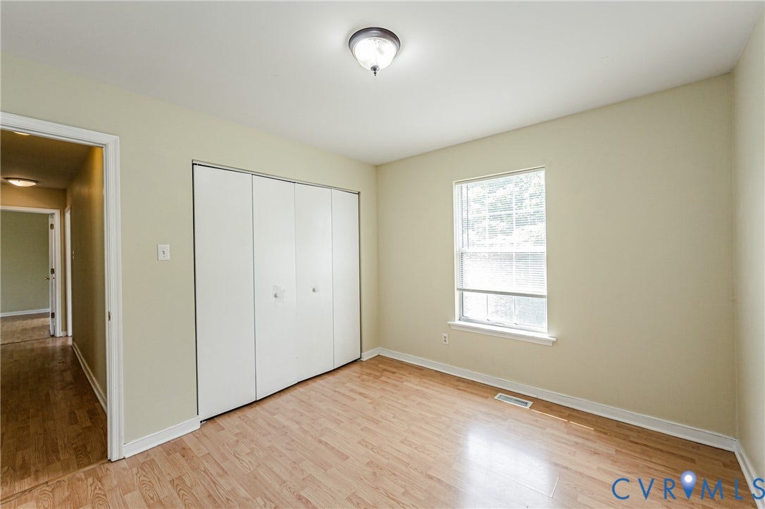Wood-finish flooring, white bi-fold closet doors, single window, and a ceiling-mounted light fixture