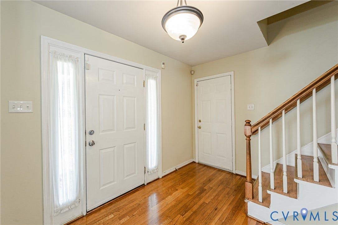 Entry foyer with wood-finish flooring, a classic staircase with wood banister, and a paneled entry door with sidelights