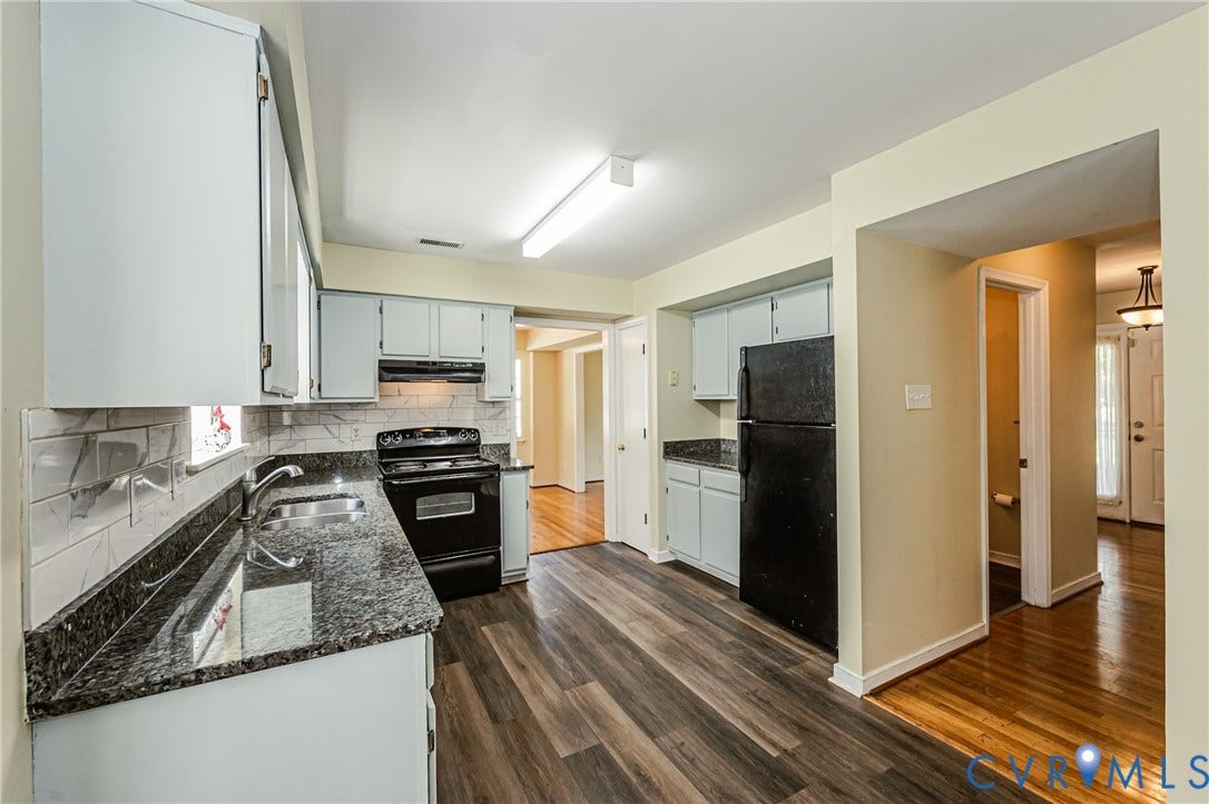 Kitchen featuring wood-finish flooring, light-toned cabinetry, dark countertops, white subway tile backsplash, and a black appliance suite