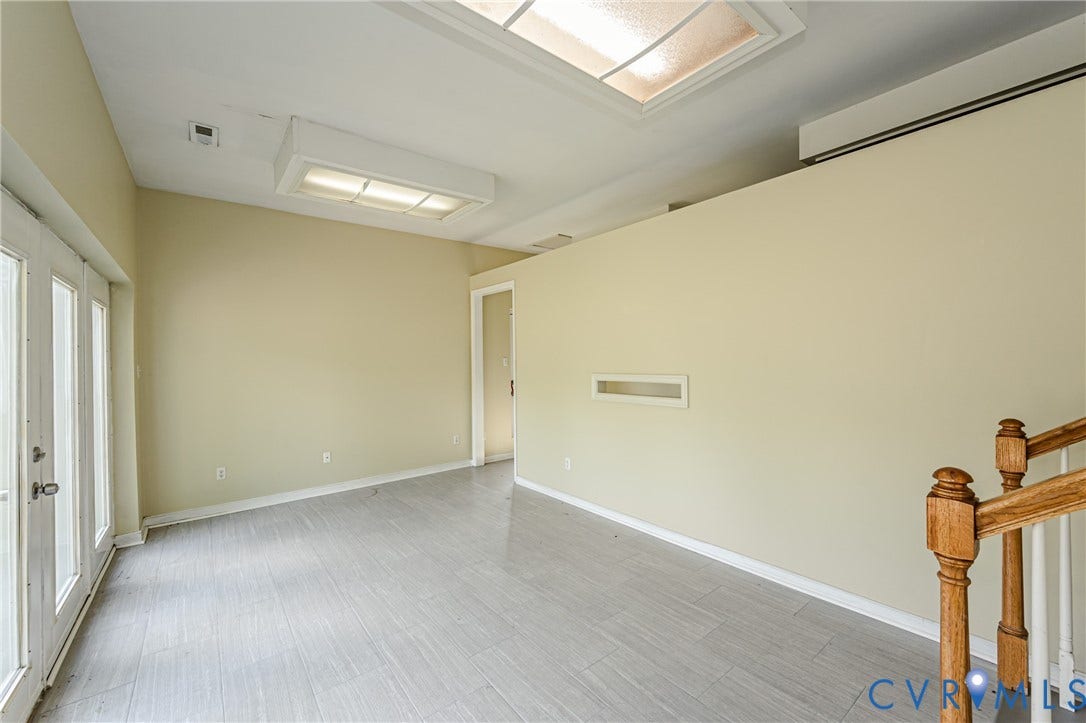 Recessed ceiling light with translucent panel, skylight, double glass-paneled doors, light grey tile flooring, and wood banister