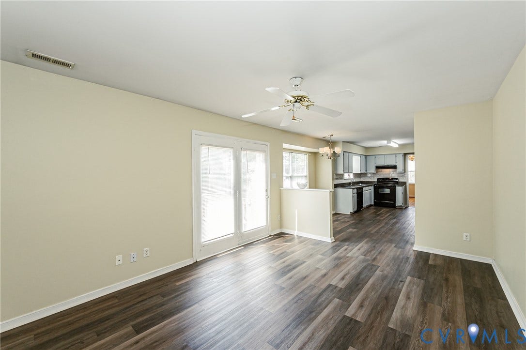 Wood-finish flooring throughout, light neutral wall paint, white ceiling fan with light kit, white French doors, and a kitchen featuring grey cabinetry and black appliances