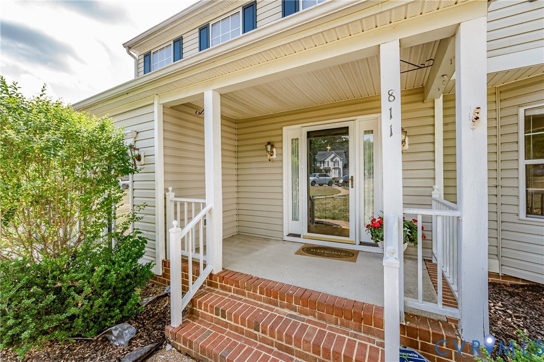 Covered entry porch featuring brick steps, white railing, and decorative outdoor lighting
