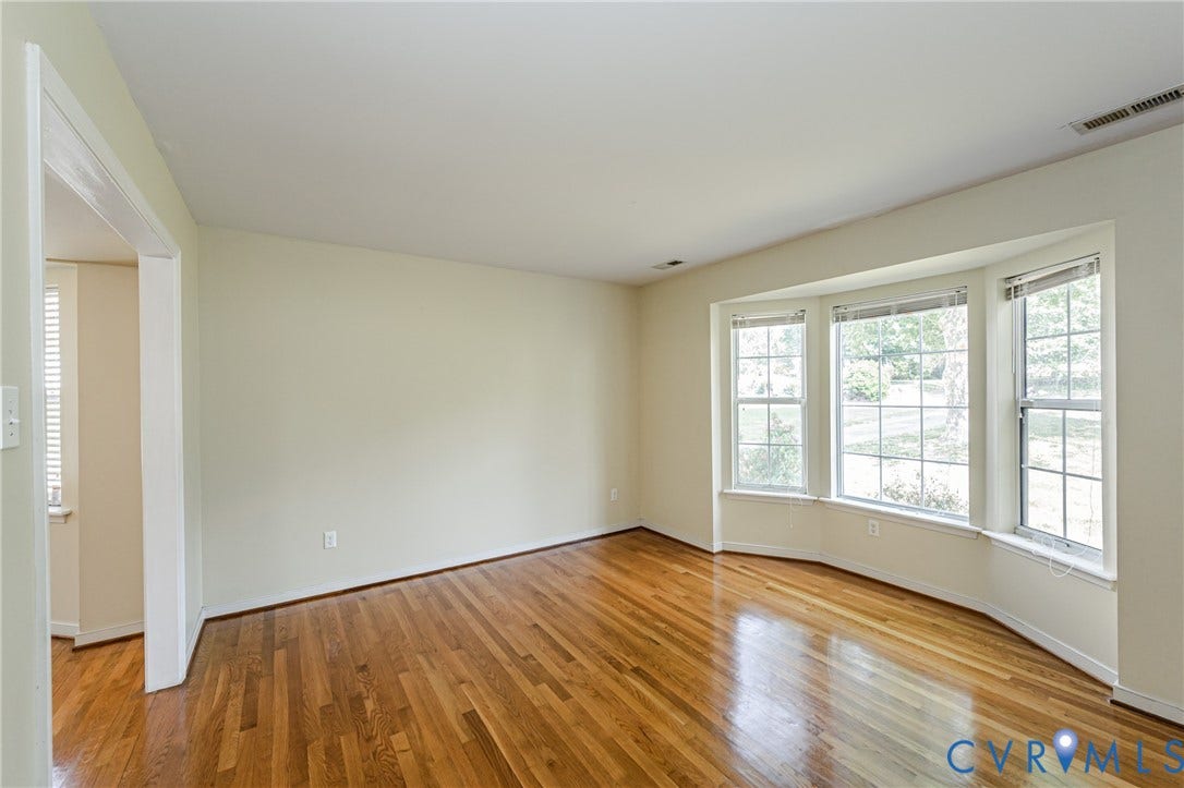 Hardwood flooring, bay window, white trim, light-colored walls, open doorway
