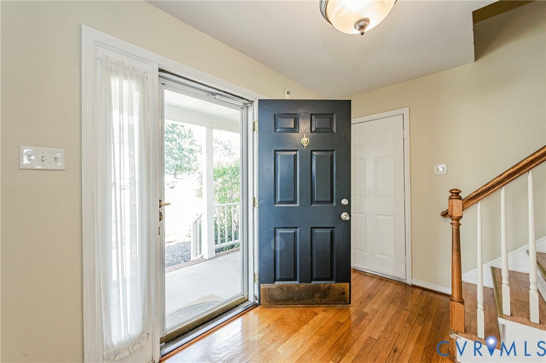 Panel-style front door, wood-finish flooring, and a staircase with wood handrails