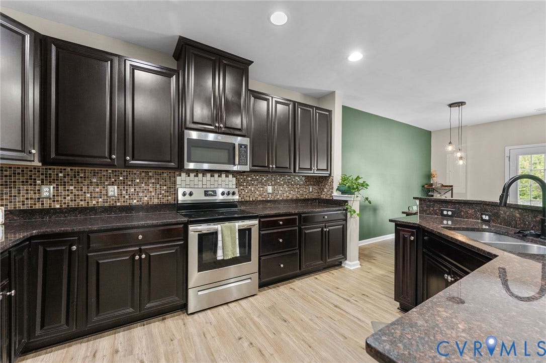 5112 Weatherby Drive, Chester, VA 23831 Wood-finish flooring, dark cabinetry, mosaic tile backsplash, built-in stainless steel appliances, and a kitchen island with sink