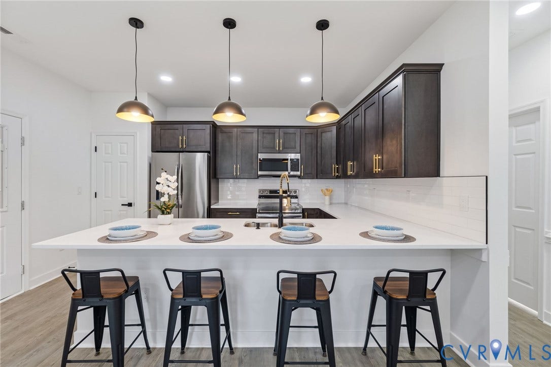 524 Cameron Street, Petersburg, VA 23803 Kitchen featuring dark wood-finish cabinetry, stainless steel appliances, a white subway tile backsplash, and a large island with a light-toned countertop and pendant lighting