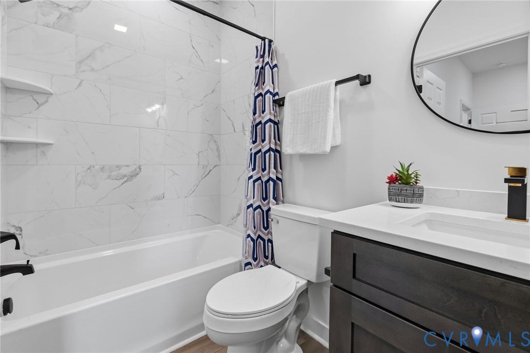 524 Cameron Street, Petersburg, VA 23803 White subway tile with subtle grey veining, built-in tub with matte black fixtures, dark wood-finish vanity with a white countertop, rectangular undermount sink, and a circular black-framed mirror