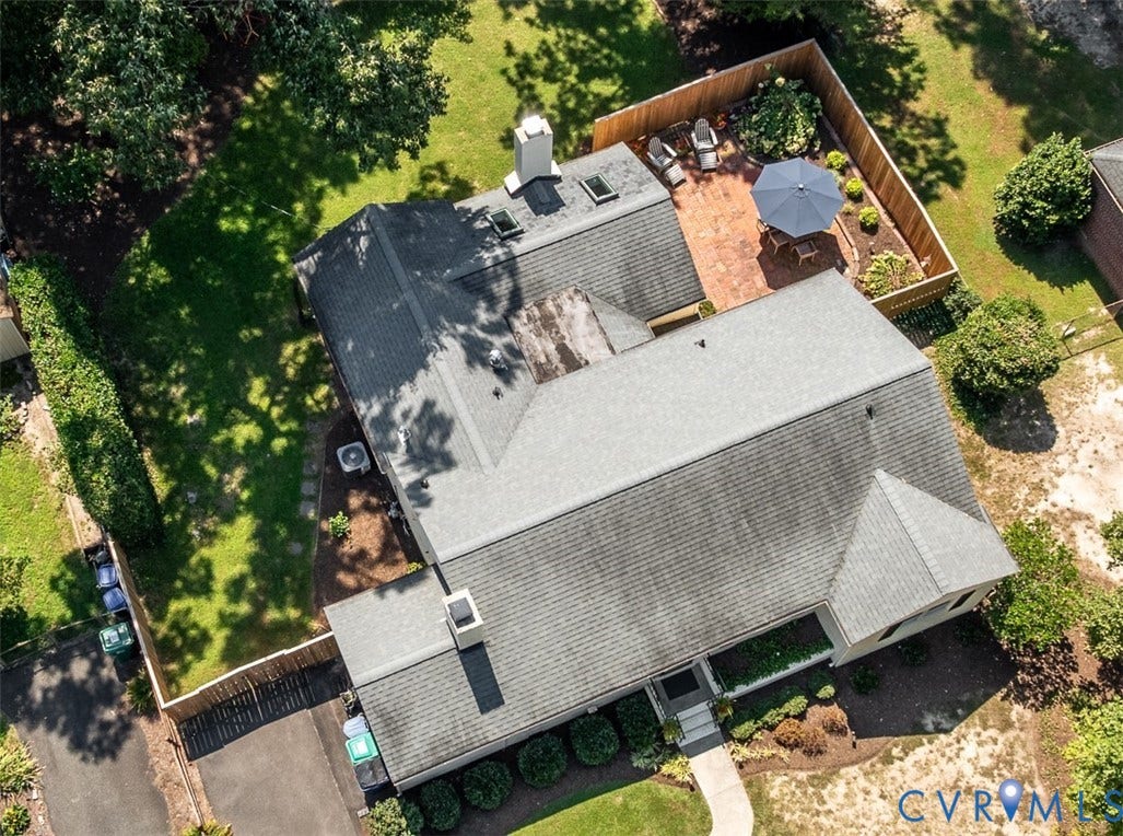 Asphalt shingle roofing, brick patio, privacy fencing, multiple chimneys, and mature landscaping