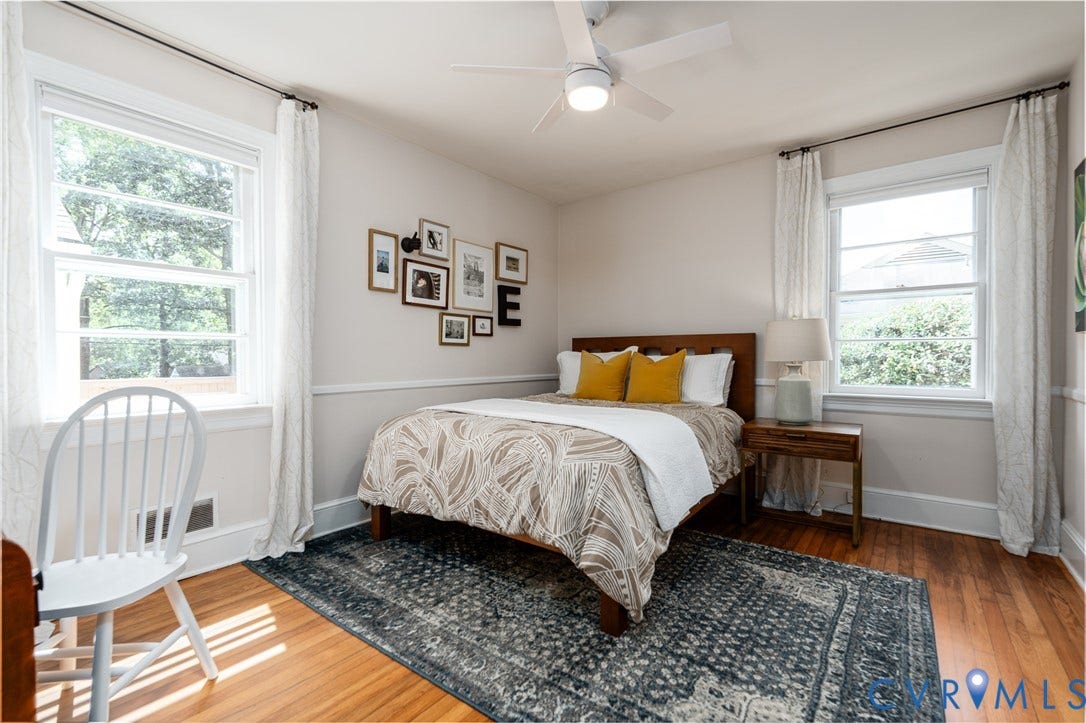 Hardwood flooring, painted trim detail, two large windows, white ceiling fan, and light-toned wall paint