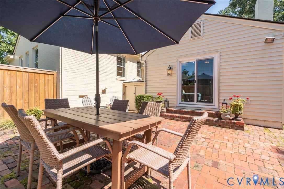 Brick paver patio featuring a sliding glass door, exterior wall lantern, and a wooden privacy fence