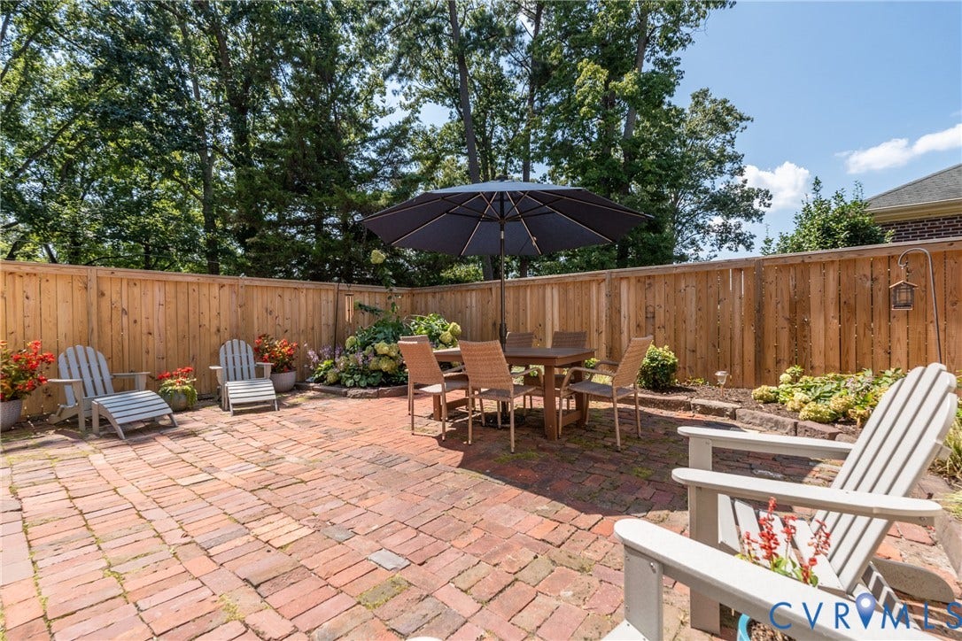 Expansive brick paver patio featuring a privacy fence, mature trees, and landscaped planting beds