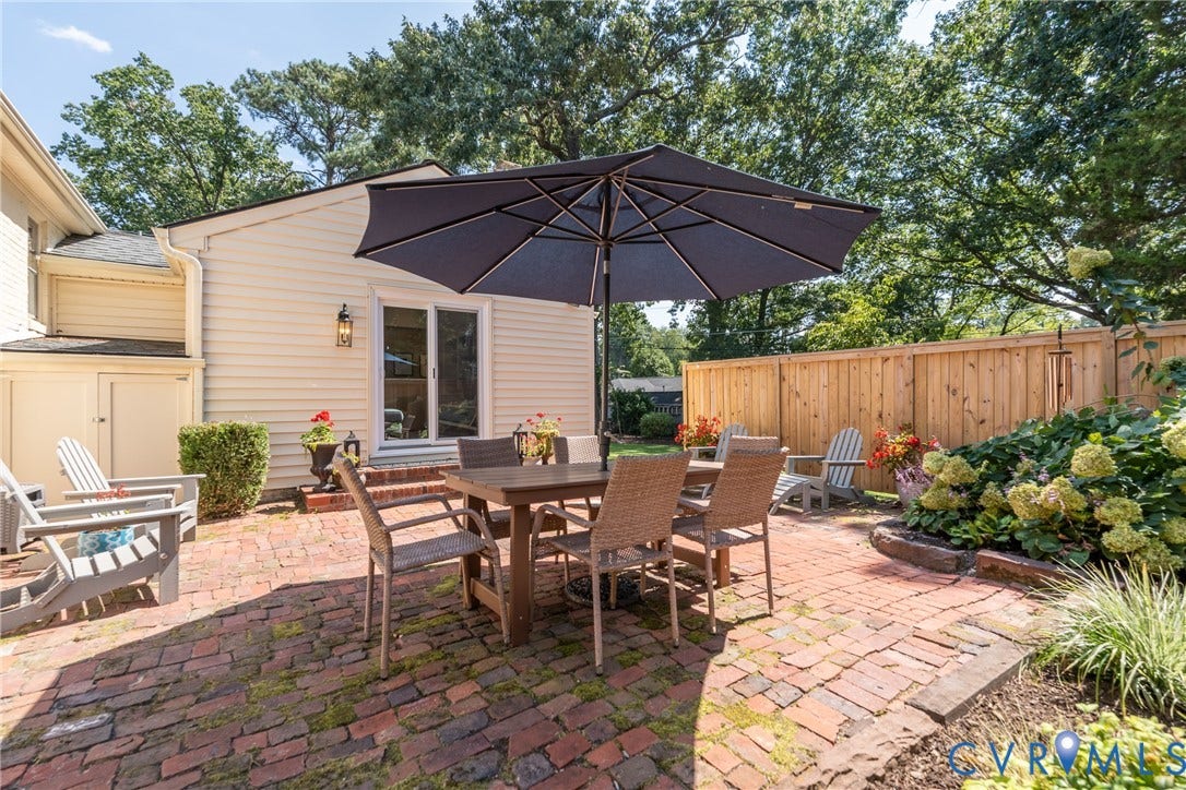 Brick paver patio with a wood privacy fence, featuring a sliding glass door entry and exterior wall sconce
