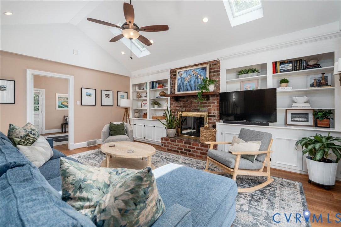 Vaulted ceiling with skylights, wood-finish flooring, brick fireplace, built-in shelving, and recessed lighting