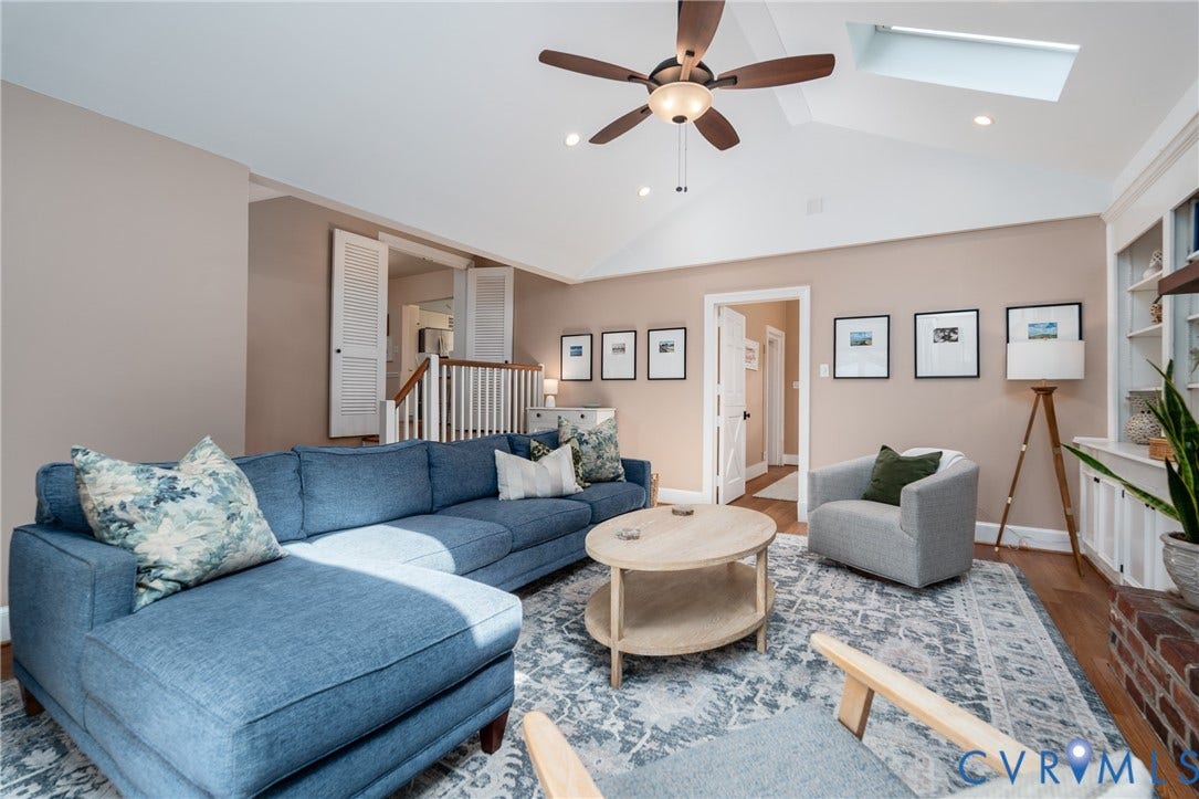 Vaulted ceiling with skylight, wood-finish flooring, built-in shelving, white baluster staircase, and interior doors with louvered details