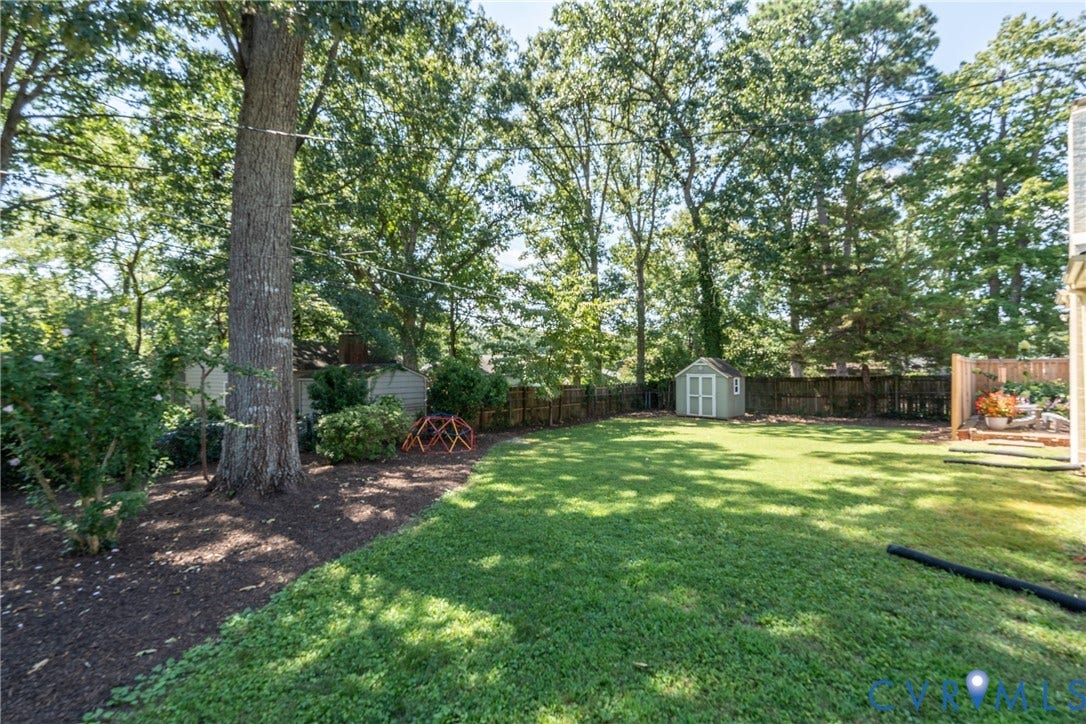 Expansive backyard featuring a manicured lawn, mature trees, wood fencing, and an outdoor storage shed