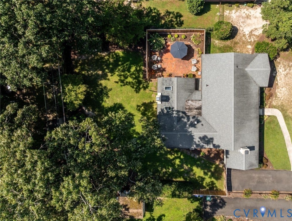 Shingle roof, multiple skylights, paved driveway, concrete walkway, and a brick patio with perimeter landscaping
