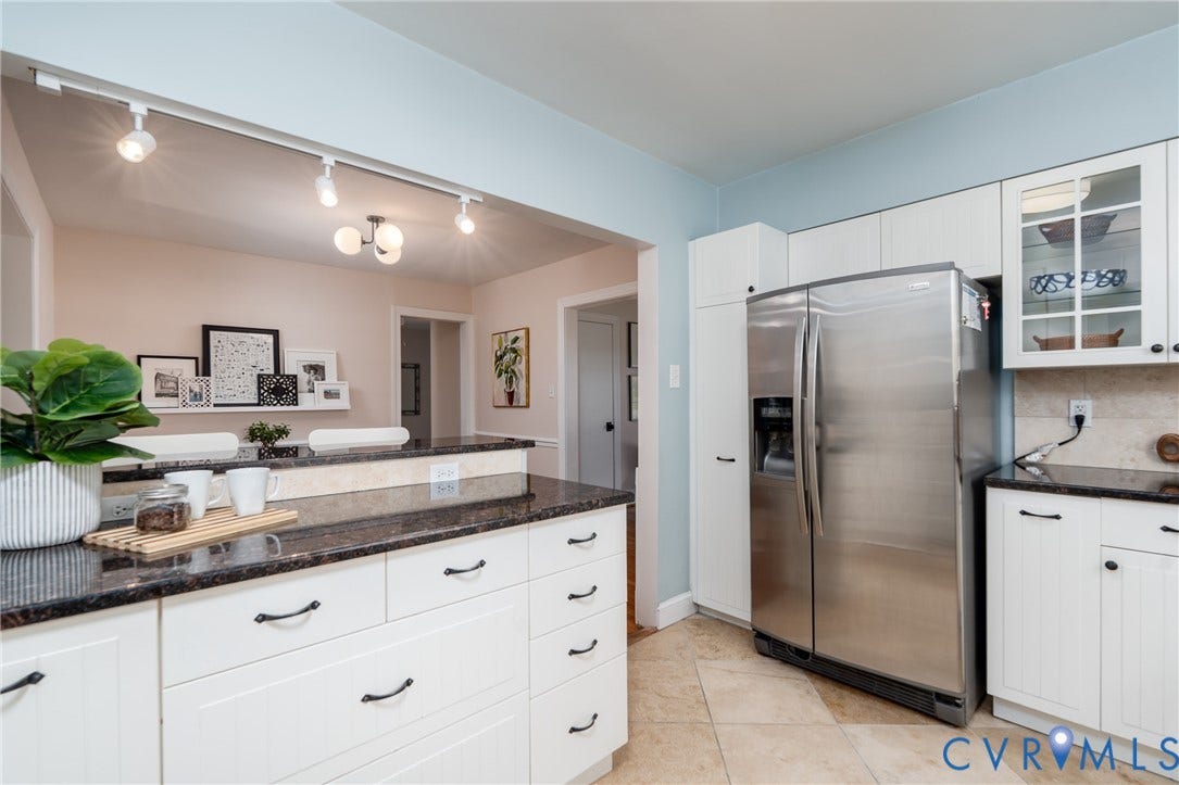 White cabinetry with black pulls, dark granite-finish countertops, stainless steel refrigerator, and tiled flooring
