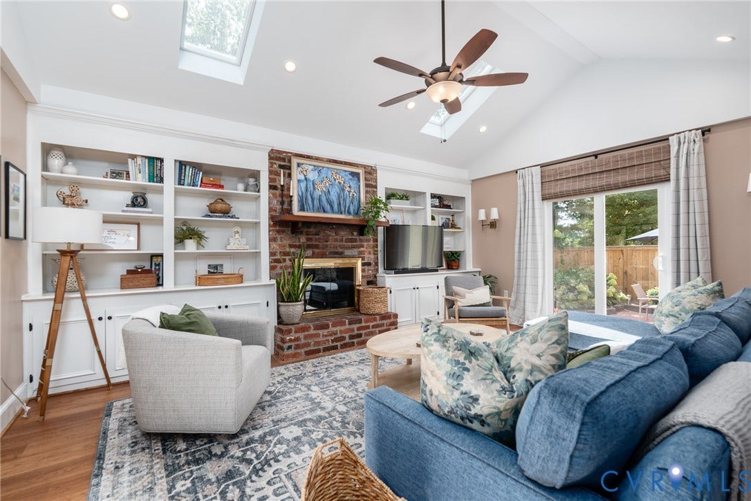 Vaulted ceiling with skylights, built-in shelving, brick fireplace, wood-finish flooring, and sliding glass doors