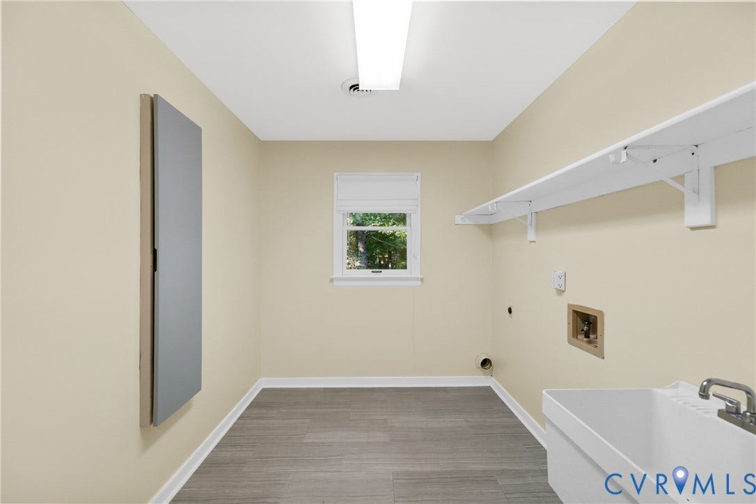 Utility room featuring wood-finish flooring, a utility sink, wall-mounted shelving, and a single window