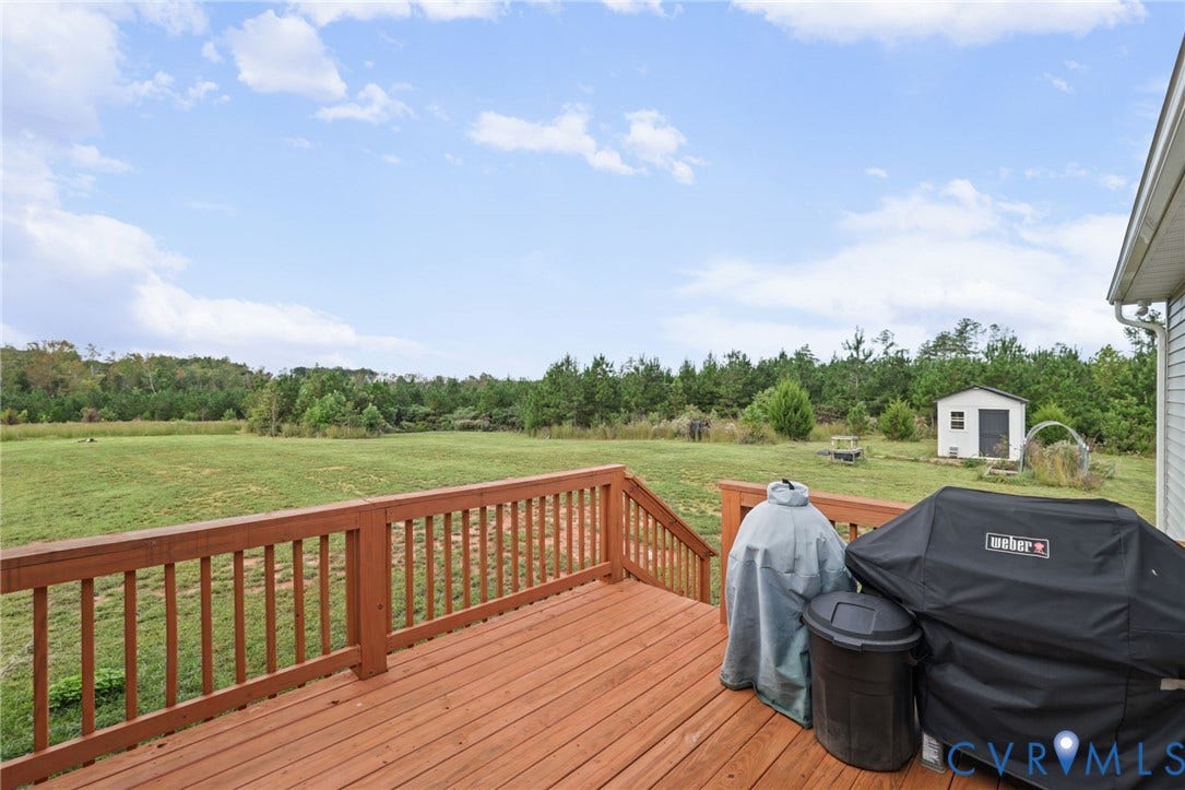 Expansive outdoor deck with wood railings, featuring a verdant grass lawn and distant tree line