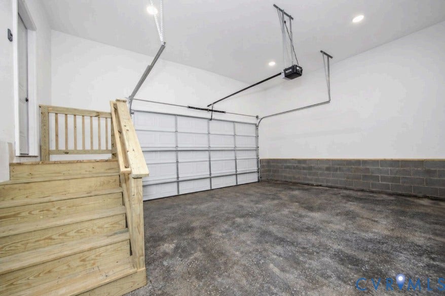Spacious garage featuring a concrete floor, block wall, and wooden staircase with railing