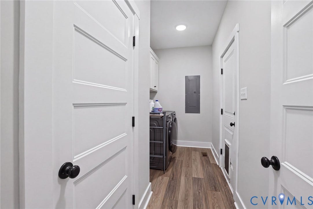 Hallway with wood-finish flooring, white paneled doors, and matte black hardware