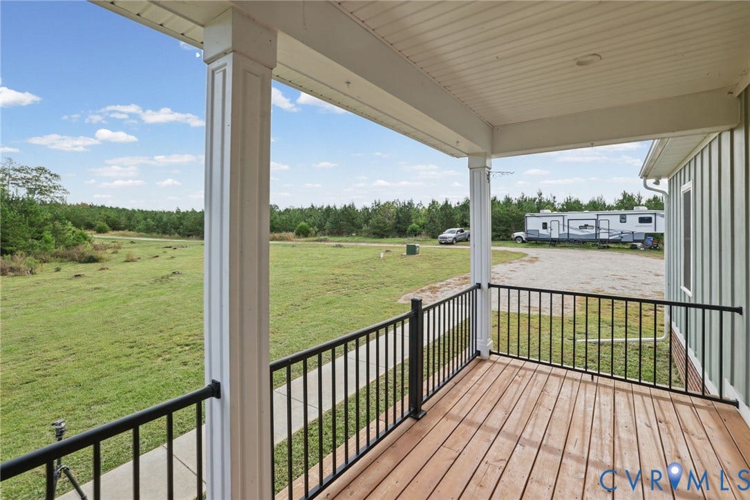 Covered porch with wood-finish decking, black metal railings, and fluted columns